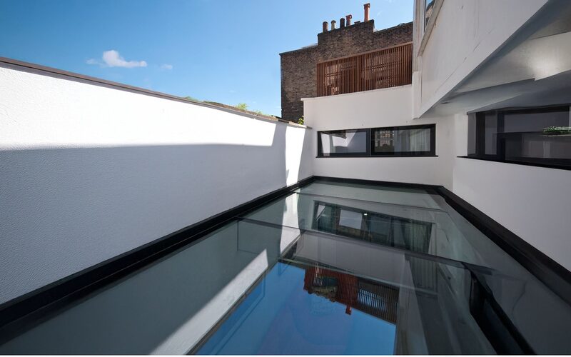 an external view of a structural glass roof spanning between two white render walls in LA - glass roofs